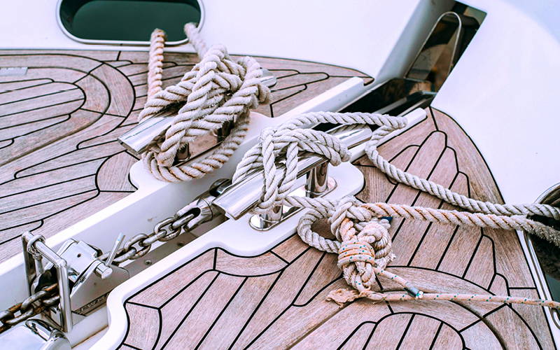 Detailopname van de boeg van een boot met houten dek, waarop meerdere dikke meertrossen netjes om roestvrijstalen klampen zijn gelegd. Er is ook een ankerketting zichtbaar die door een ankerlier loopt. Detailopname van de boeg van een boot met houten dek, waarop meerdere dikke meertrossen netjes om roestvrijstalen klampen zijn gelegd. Er is ook een ankerketting zichtbaar die door een ankerlier loopt.