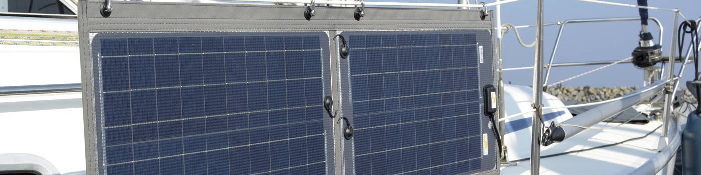 Zwei Solarpanele sind seitlich an einem Segelboot montiert und in Richtung Sonne ausgerichtet. Die Panele sind auf einem klappbaren Aluminiumrahmen befestigt, der am Heckkorb des Bootes angebracht ist Zwei Solarpanele sind seitlich an einem Segelboot montiert und in Richtung Sonne ausgerichtet. Die Panele sind auf einem klappbaren Aluminiumrahmen befestigt, der am Heckkorb des Bootes angebracht ist