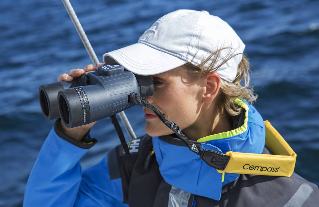 Vrouw met marineverrekijker op een zeilboot – uitkijk bij ruwe zee met drijfriem Vrouw met marineverrekijker op een zeilboot – uitkijk bij ruwe zee met drijfriem
